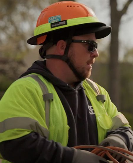 Construction worker in neon jacket holds cables outdoors.