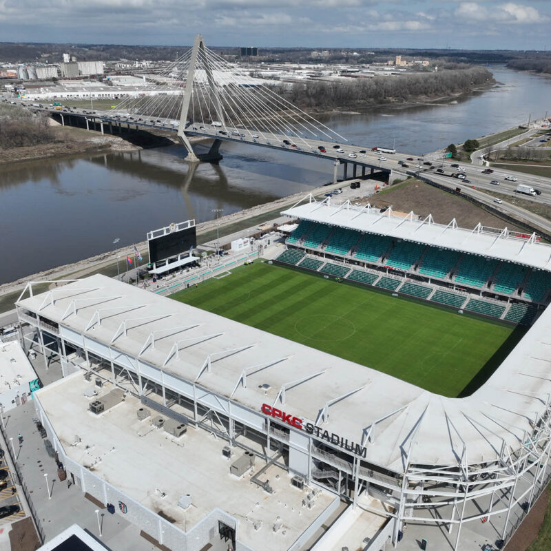 Aerial of CPKC Stadium, green field, parking, river, bridge.