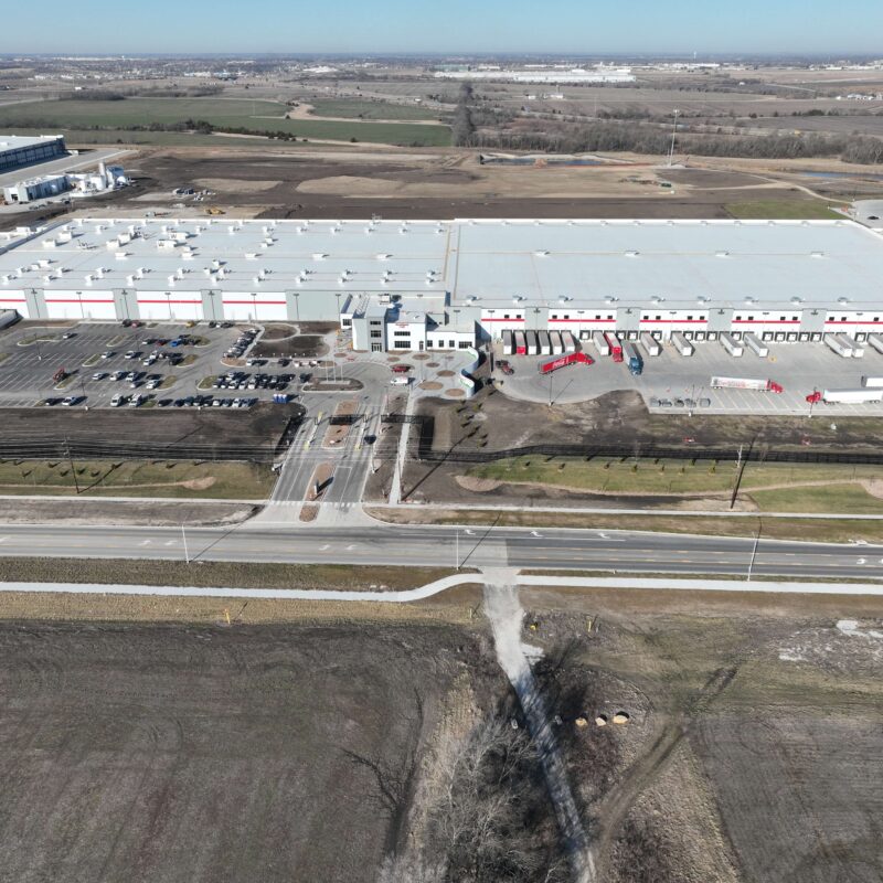 Aerial view of an industrial warehouse, trucks, parking, and fields.