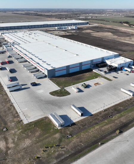 Aerial view of a warehouse, loading docks, trucks, and fields.