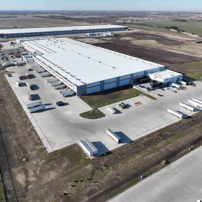Aerial view of a warehouse, loading docks, trucks, and fields.