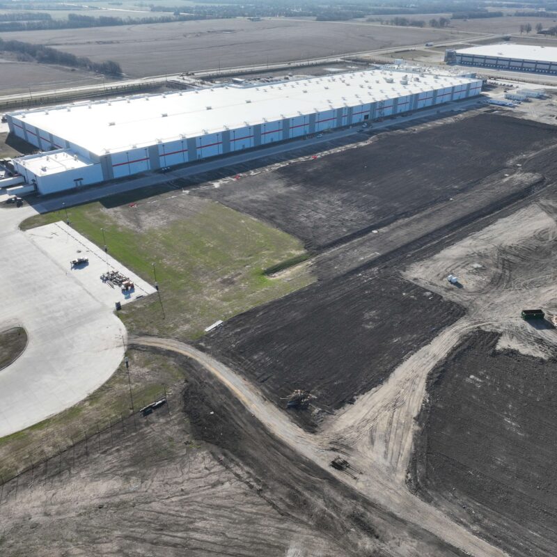 Aerial view of warehouse, nearby parking, and dirt lots.