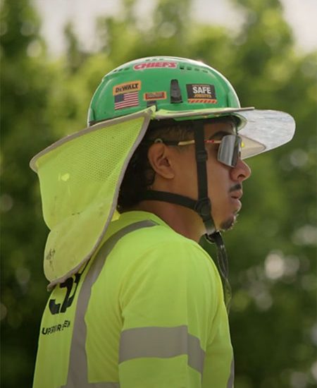 Worker in neon yellow shirt and green hard hat outdoors.