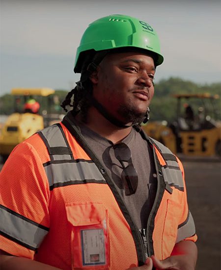 Man in orange safety vest and green hard hat at construction site.