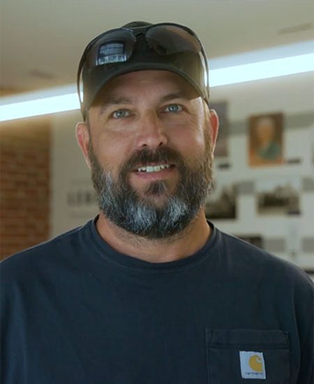 Bearded man in cap and navy shirt indoors, photos blurred.