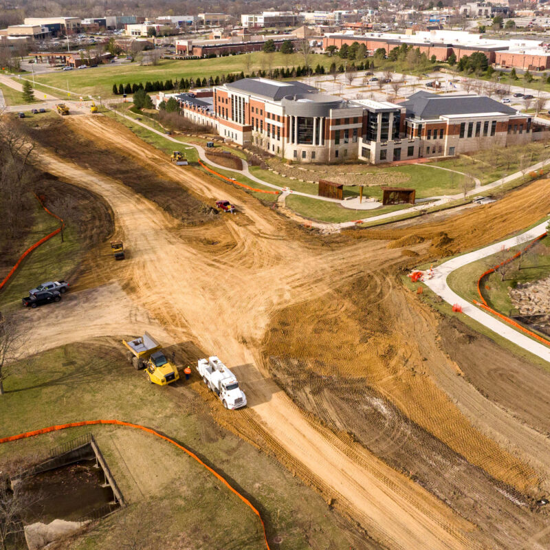 Aerial shot of construction, machines, building, woods, and water.