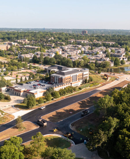 Aerial view: new road by modern buildings, with trees nearby.