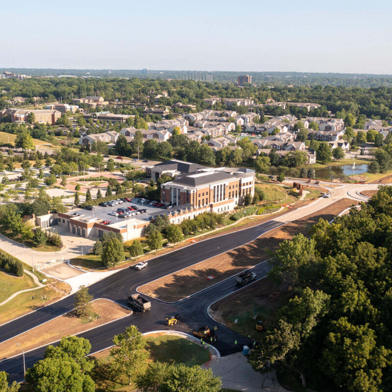 Aerial view: suburb, new road, building, trees, parking lots.