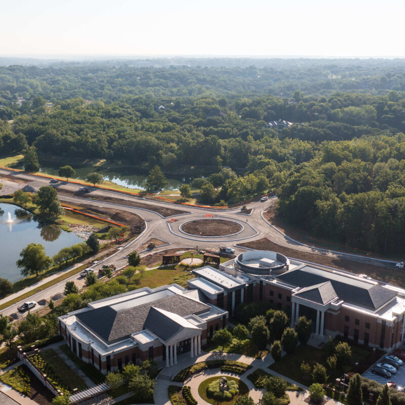 Roundabout construction site beside offices, roads, lots, and trees.