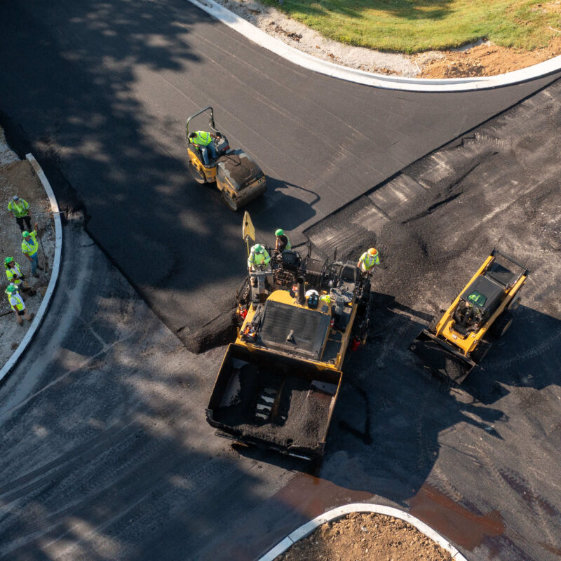 Aerial view of workers paving and smoothing asphalt road.