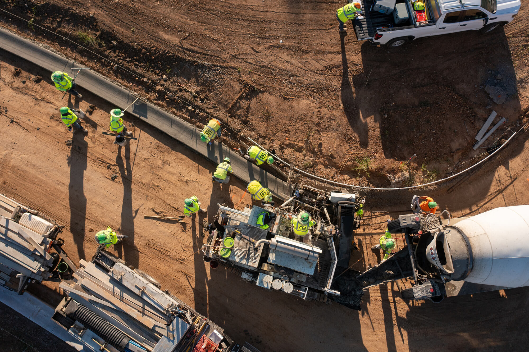 Workers in vests pour concrete on curved road from above.