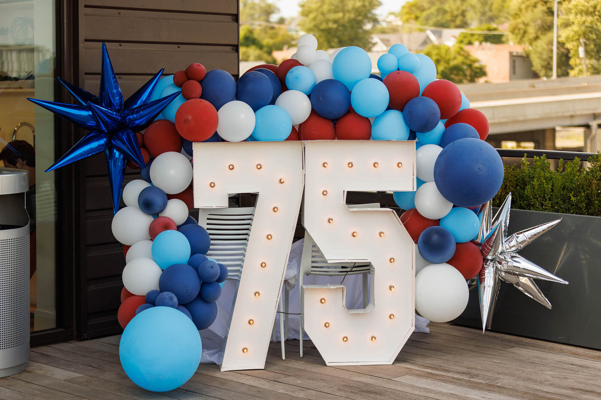 Lit 75 sign with red, white, blue balloons and stars.