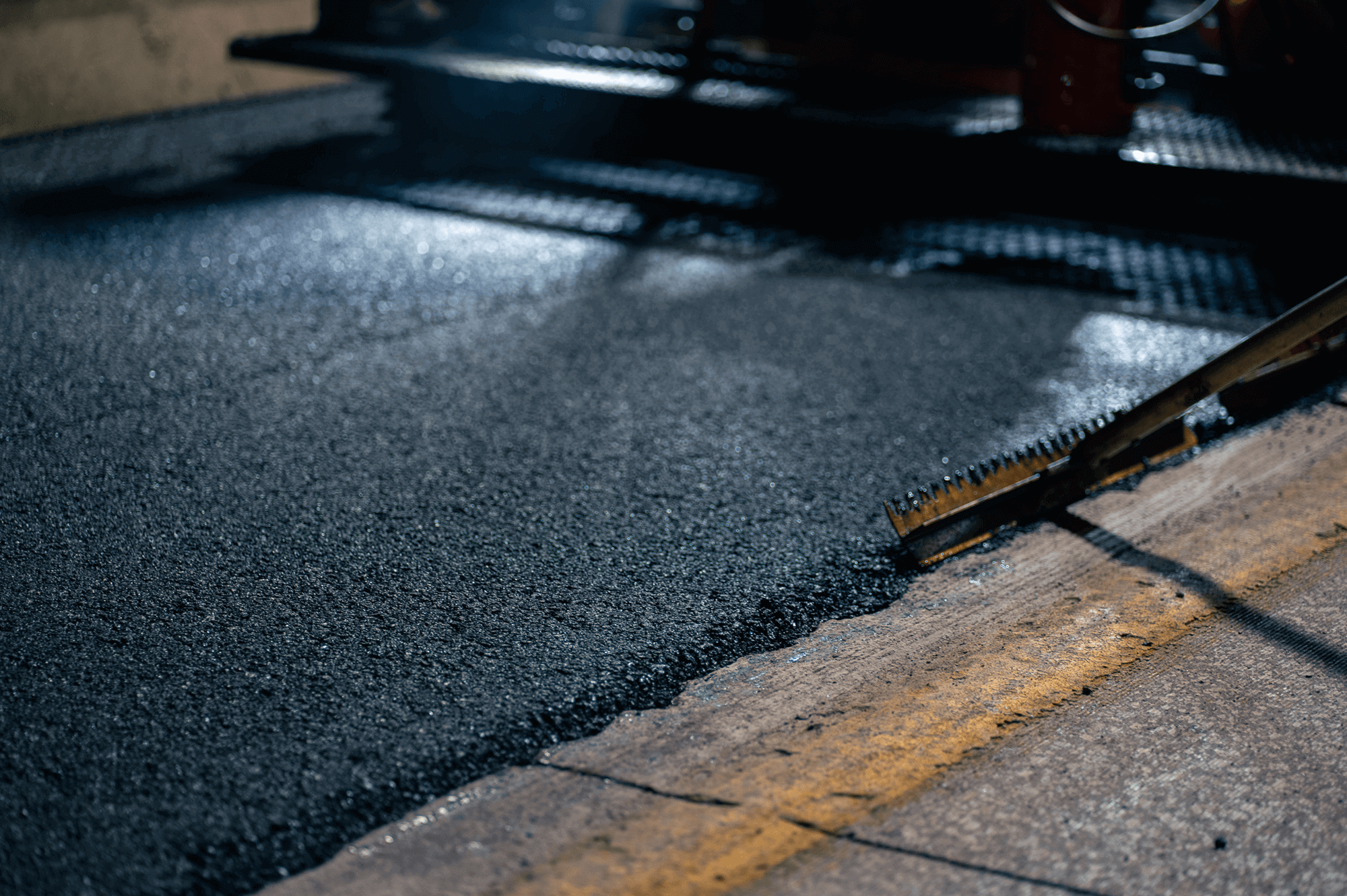 Fresh asphalt spread next to old pavement with yellow line.