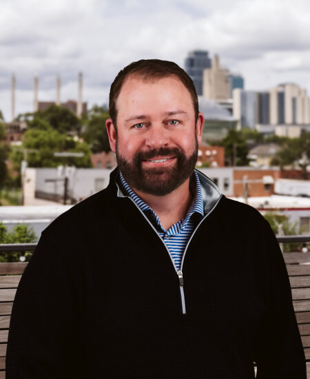 Bearded man in dark sweater outside with urban skyline.