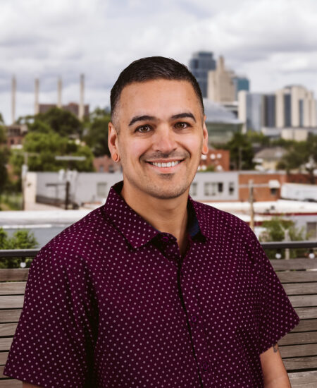Smiling man in maroon shirt sits on a bench outdoors.