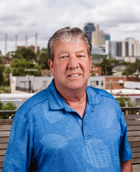 Man in blue polo stands on bench, city and clouds behind.