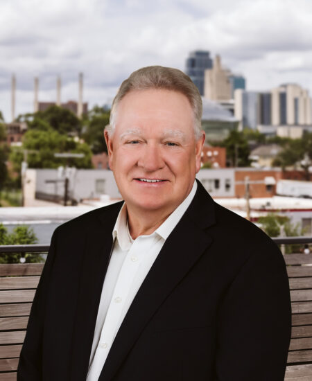 Older man in suit sits on bench with city skyline.