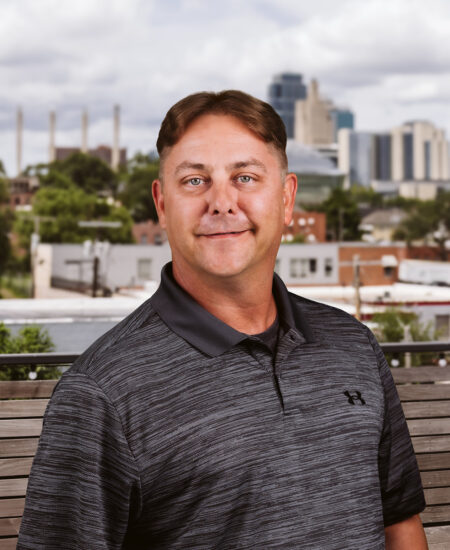 Man in dark shirt on bench with city skyline behind.
