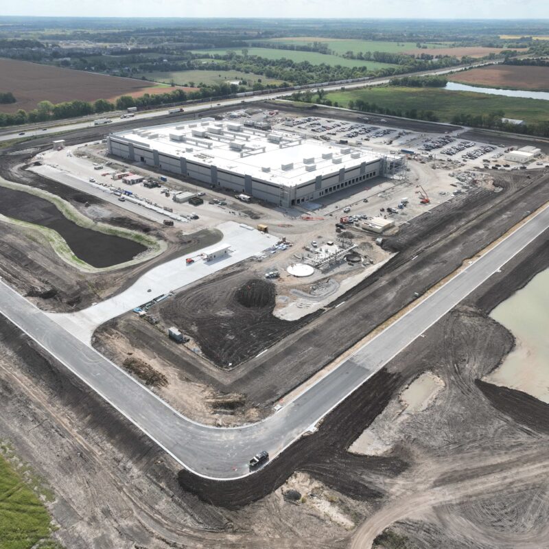 Aerial view of industrial building amid construction and parking lots.