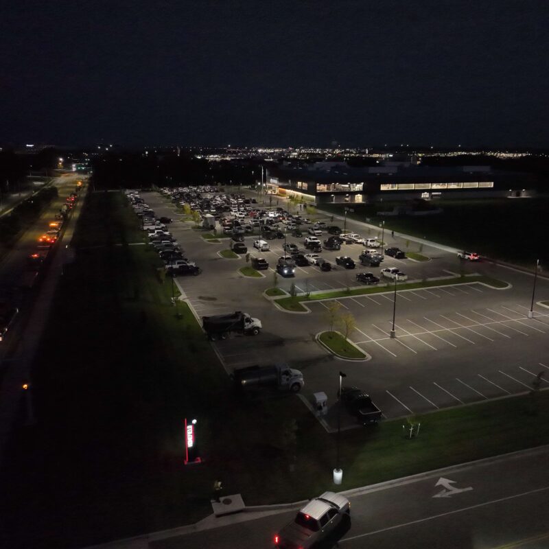 Night aerial of a mostly full, brightly lit parking lot.