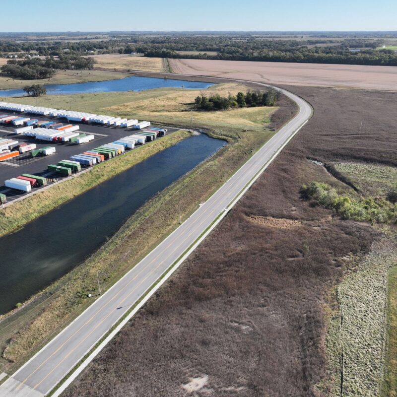 Aerial view: rural road, canal, semi-trailers, open fields.