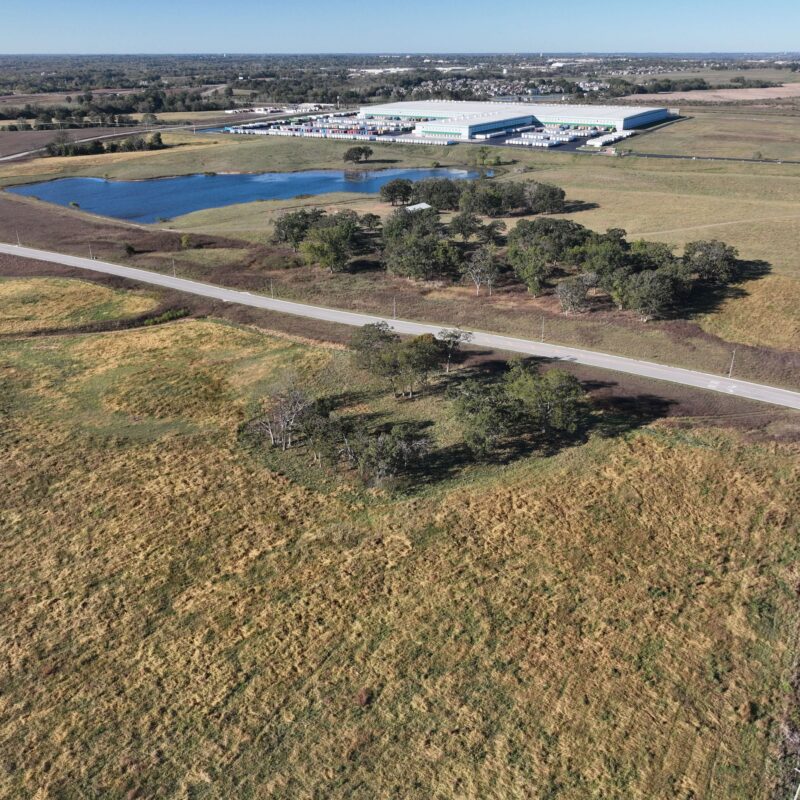 Aerial view of fields, pond, trees, road, and factory.