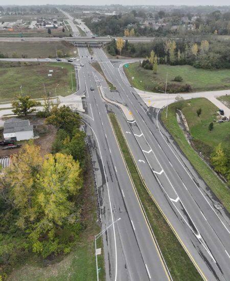 Aerial view of multi-lane highway with ramps, trees, and buildings.