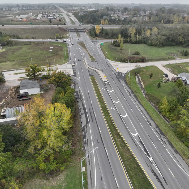 Aerial view of multi-lane highway with ramps, trees, and buildings.