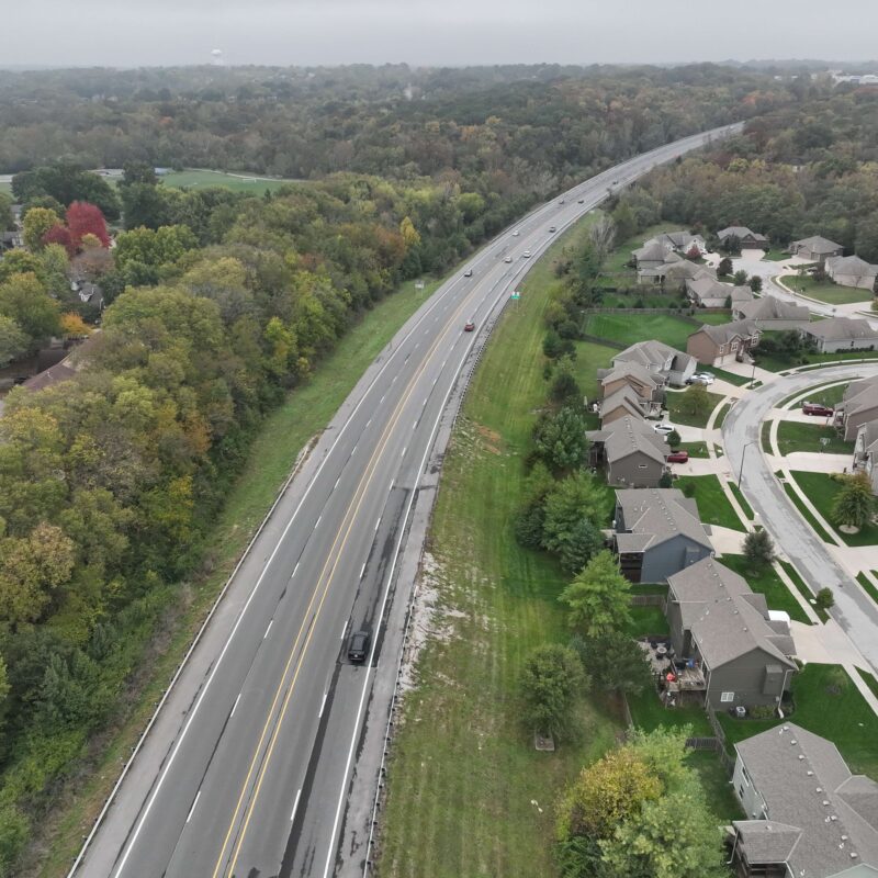 Highway beside suburban homes and trees on a cloudy day.