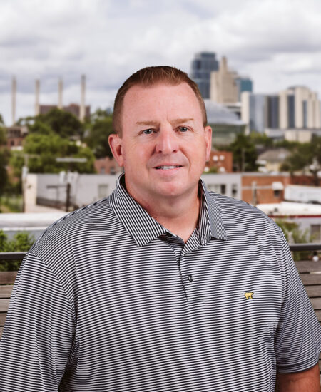 Man in striped polo shirt outdoors, city skyline behind.