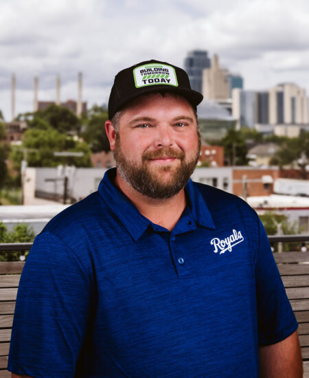 Bearded man in black hat and blue Royals shirt, city behind.