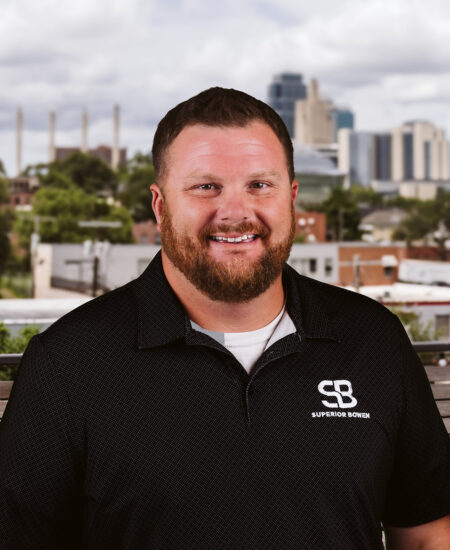 Man with beard in black polo, city skyline behind.