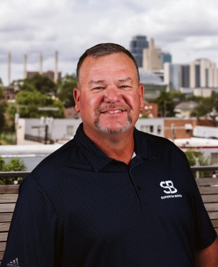 Man with short hair, goatee, and SB logo shirt outdoors.