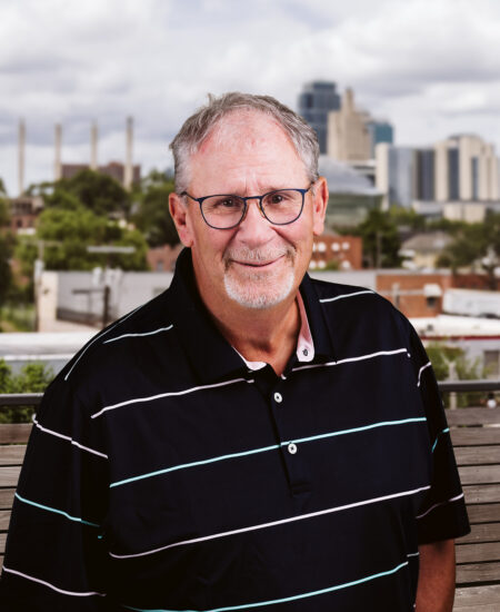 Older man with gray hair and glasses in front of city.
