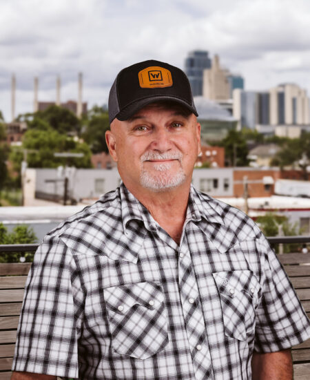 Older man in plaid shirt and cap sits on outdoor bench.