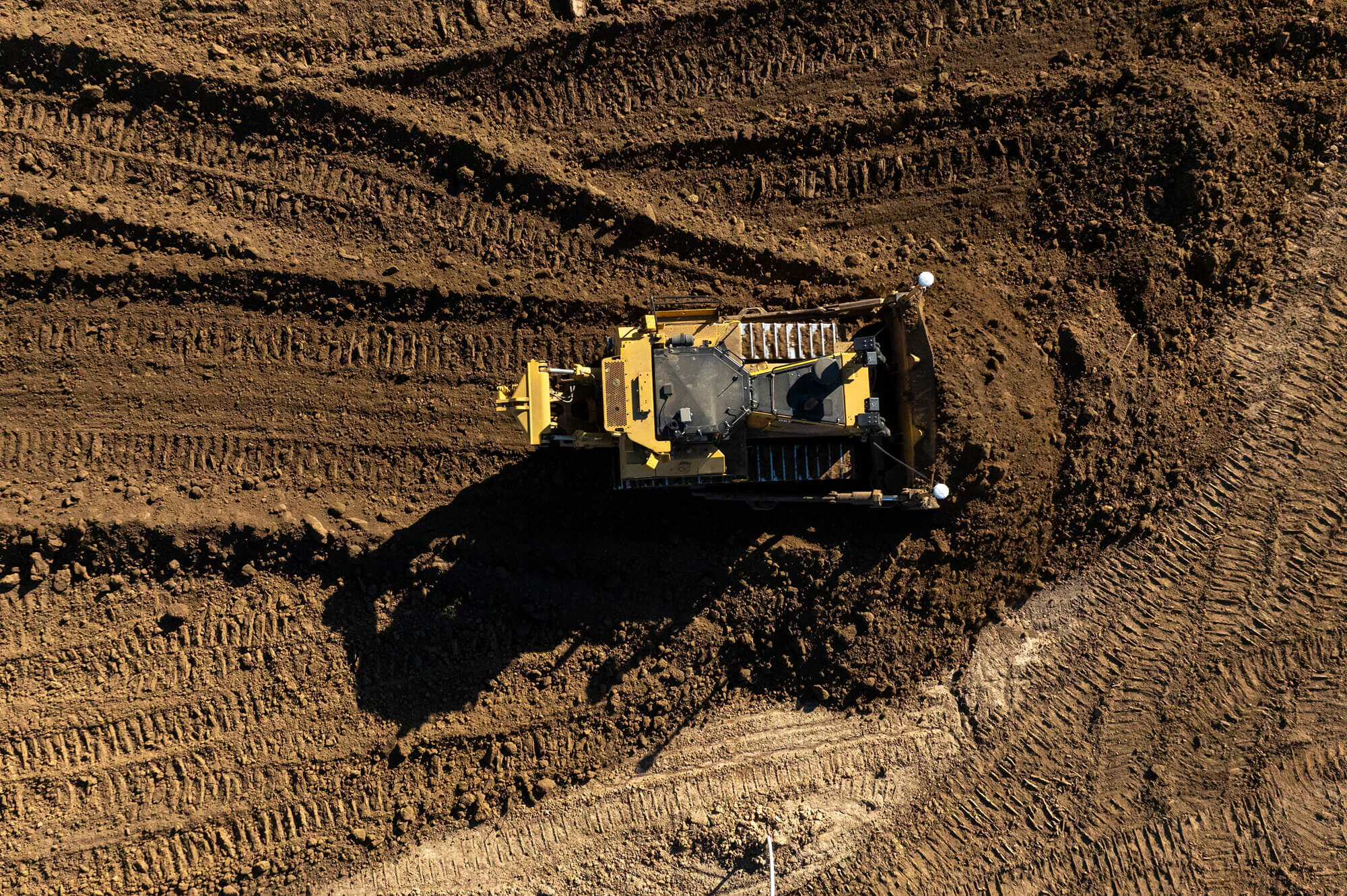 Yellow bulldozer moves dirt, leaving tracks on construction site.