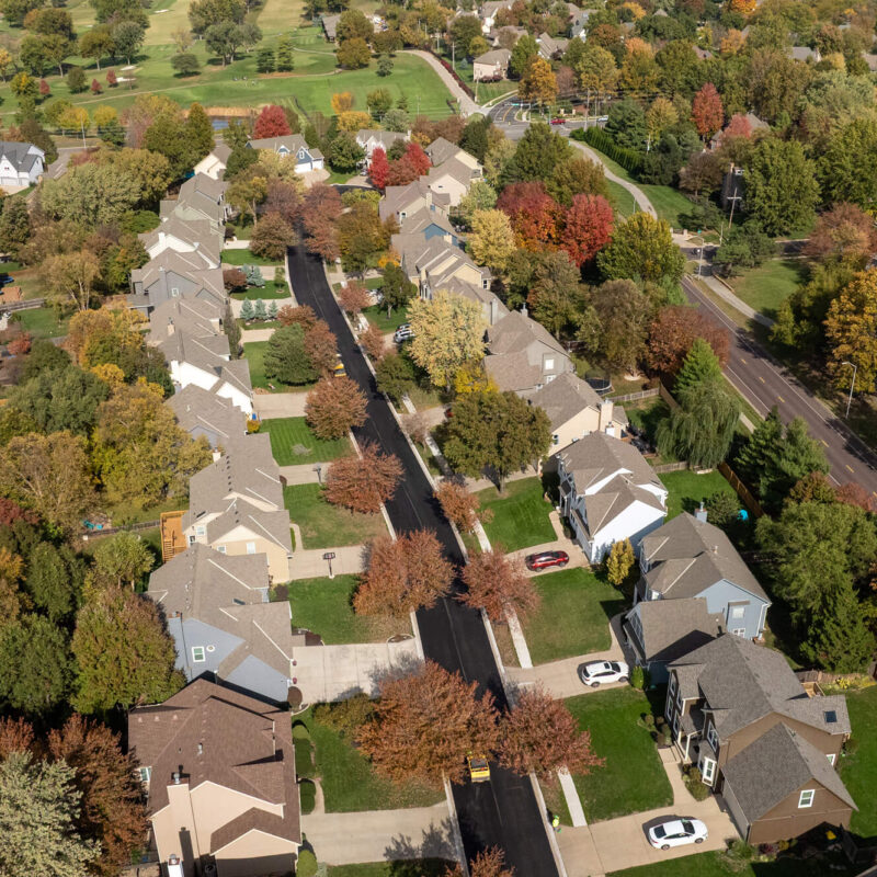 Aerial view of suburb: houses, autumn trees, road on right.