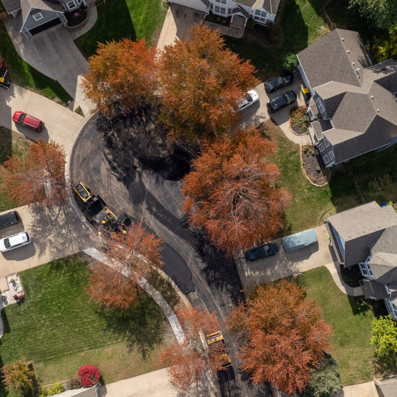 Aerial view of curved street, houses, parked cars, autumn trees.