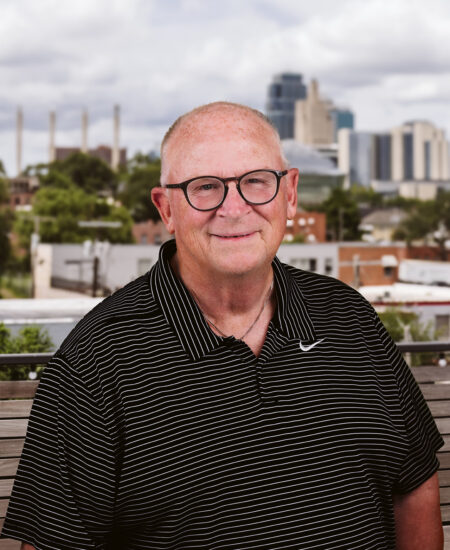 Older man with glasses and striped polo outdoors in city.