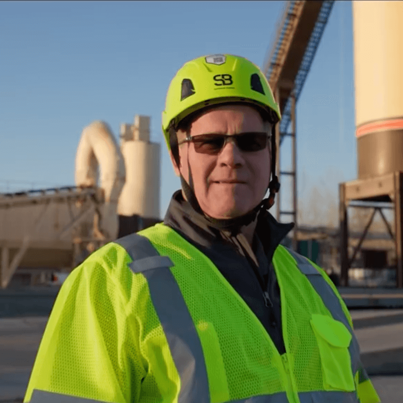 Man in neon safety jacket and helmet at industrial site.