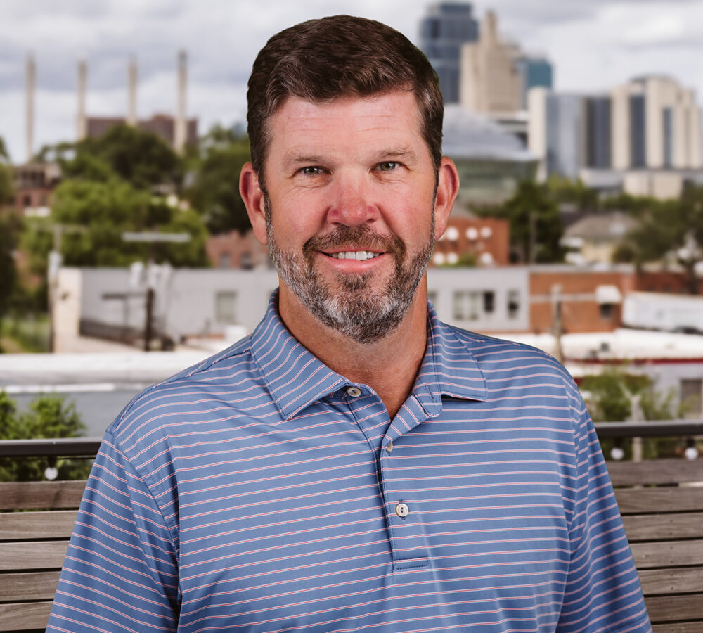 Man in blue striped polo outdoors, cityscape behind him.