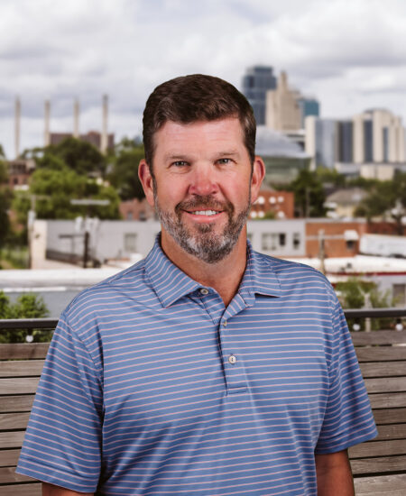 Man in blue striped polo outdoors, cityscape behind him.