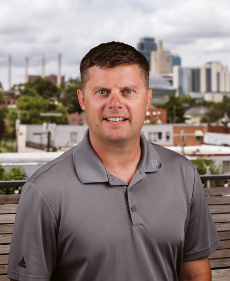 Man with short brown hair in gray polo, city behind.