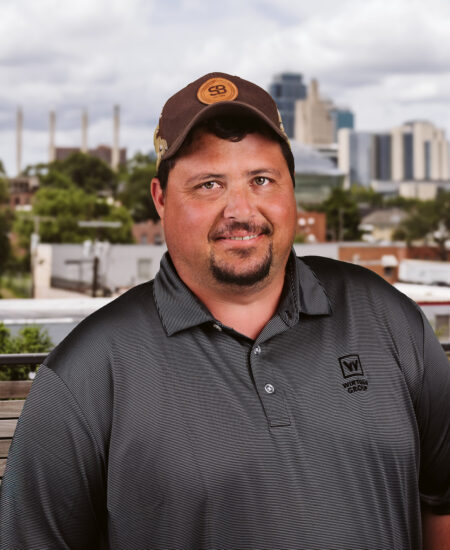 Man in brown cap and gray W shirt outdoors, city behind.