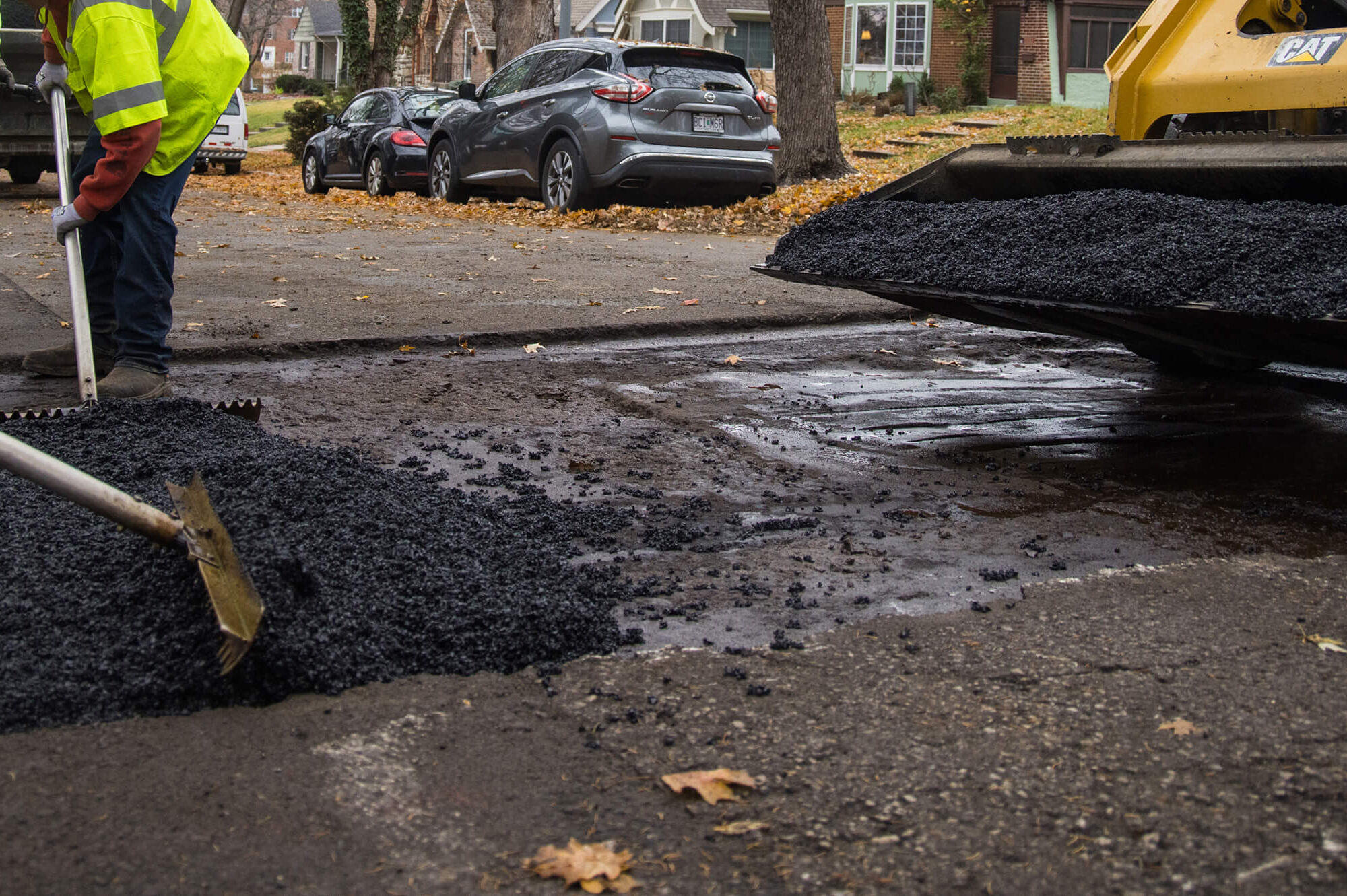 Workers use rakes and loader to repair neighborhood road.