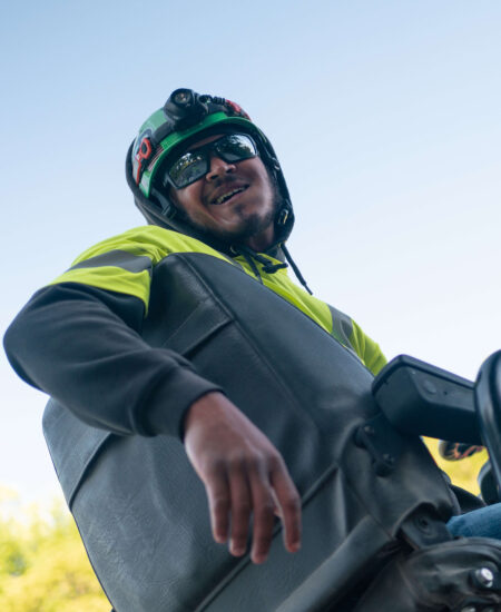 Smiling worker in safety gear sits on equipment under clear sky.