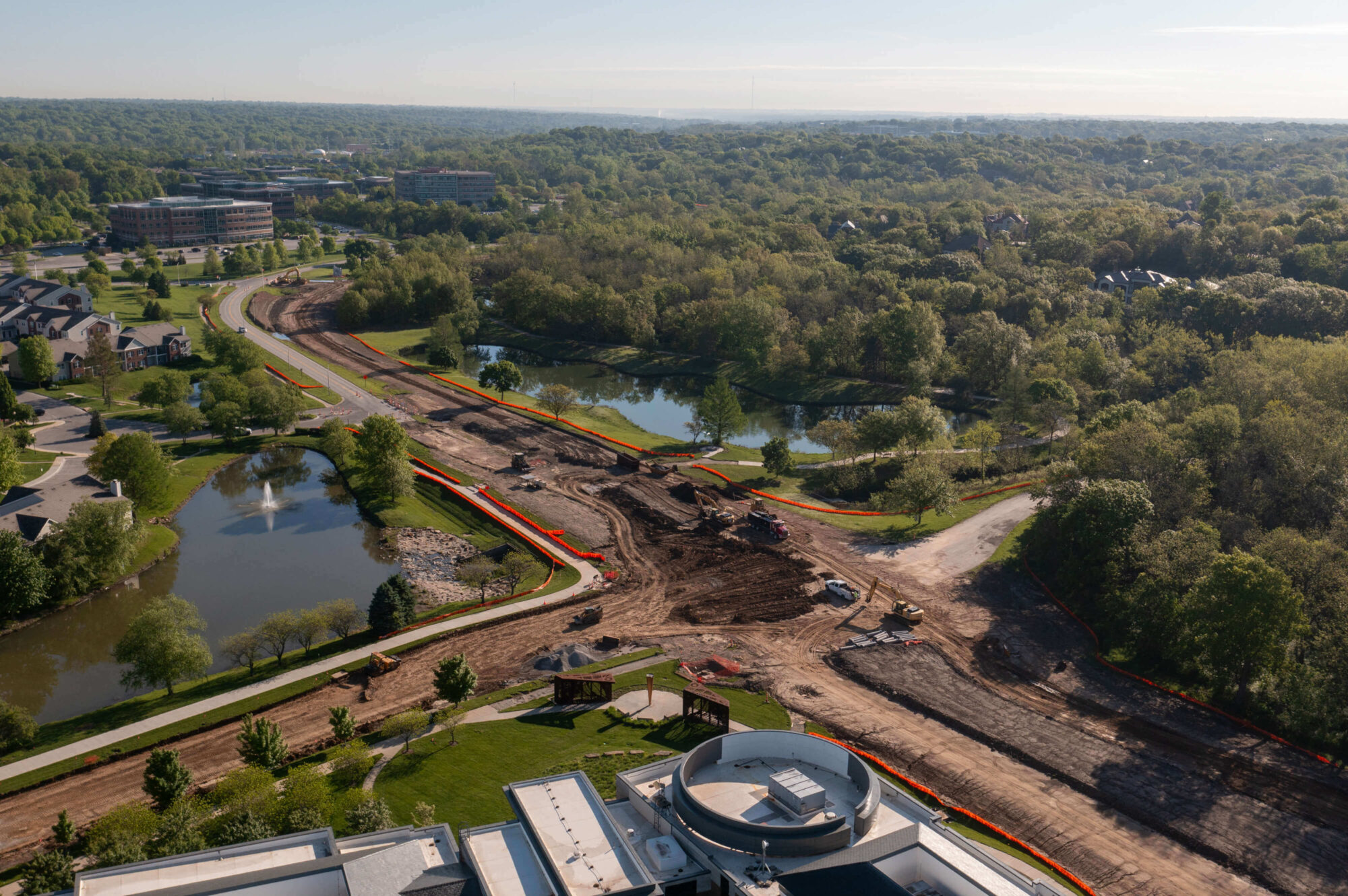 Aerial of construction site, machinery, ponds, trees, clear sky.
