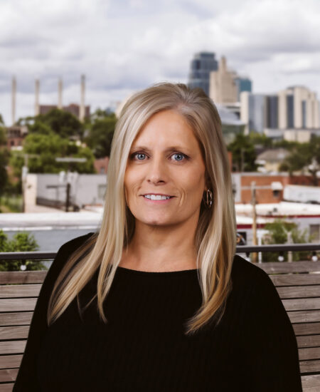 Blonde woman in black top sits on a bench outdoors.