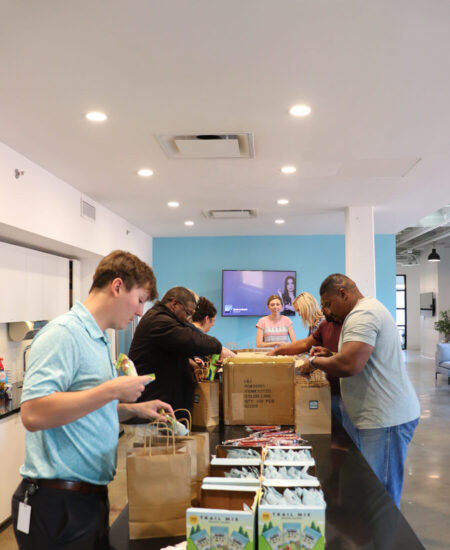 People pack snacks into paper bags in an office kitchen.