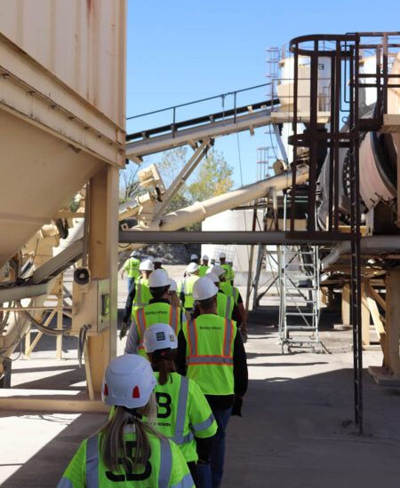 People in safety gear walk through an industrial facility.